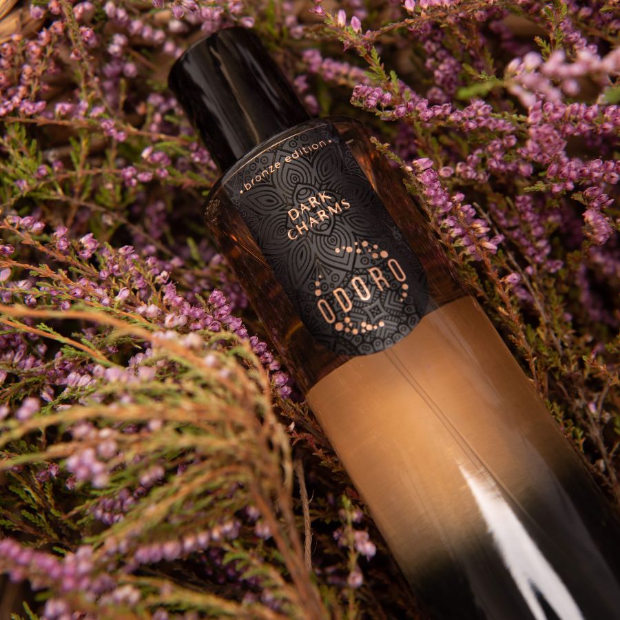 Elegant glass bottle of DARK CHARMS luxury spray fragrance lying among lavender sprigs, highlighting its floral and oriental scent.