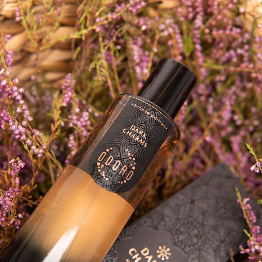 Elegant glass bottle of DARK CHARMS luxury spray fragrance lying among lavender sprigs, highlighting its floral and oriental scent.