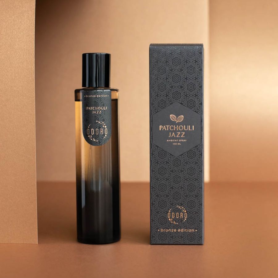 Patchouli jazz luxury spray bottle standing next to its packaging box on a nude background, showcasing its elegant design.