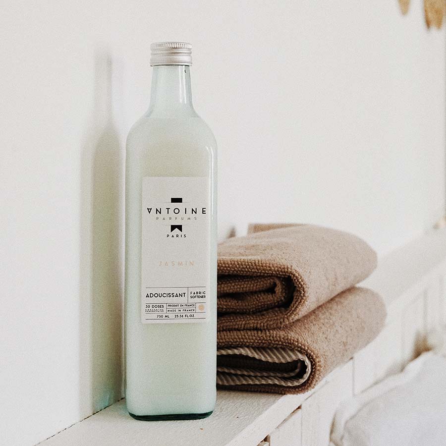 Antoine Parfums Jasmin fabric softener bottle placed beside folded beige towels, giving a fresh, clean vibe.