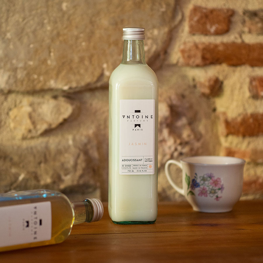 Antoine Parfums Jasmin fabric softener bottle elegantly displayed on a wooden table next to a vintage teacup.