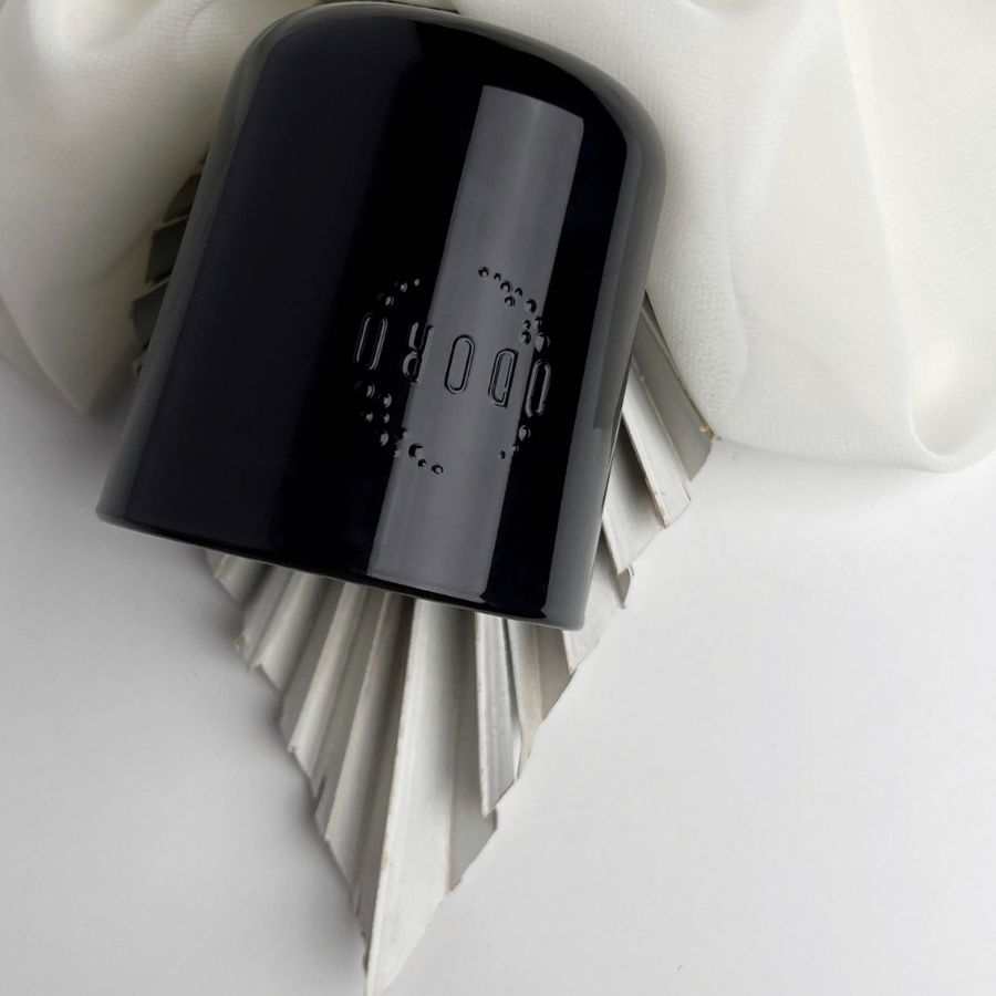 Cuban Soul candle black glass container with its lid placed upside down on a delicate white fabric.