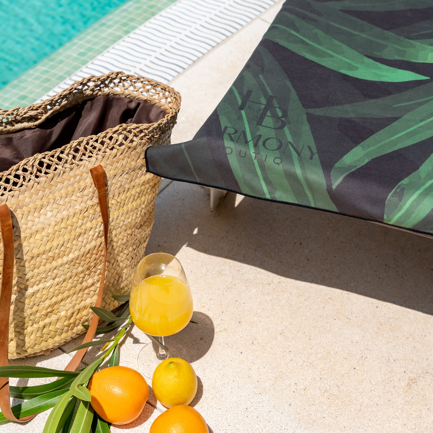 Jungle Drift beach towel on sun lounger by the pool with orange juice, citrus fruits and straw bag – tropical and refreshing summer vibe.