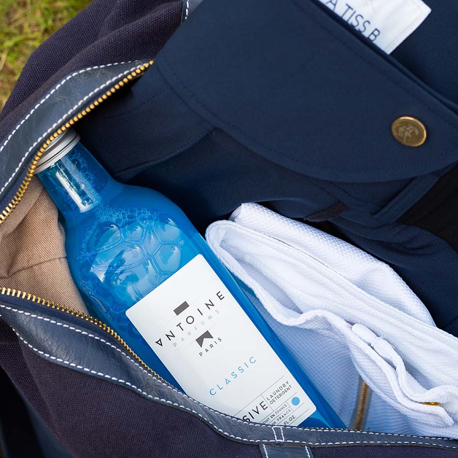 Antoine Classic perfumed laundry detergent in a glass bottle, placed inside a bag with folded clothes.