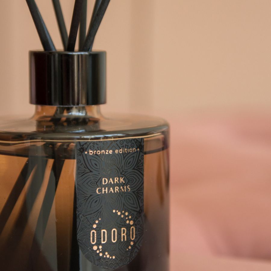 Close-up of a brown home fragrance bottle featuring the Odoro 'DARK CHARMS' label, highlighting its elegant design and rich color against a neutral background.