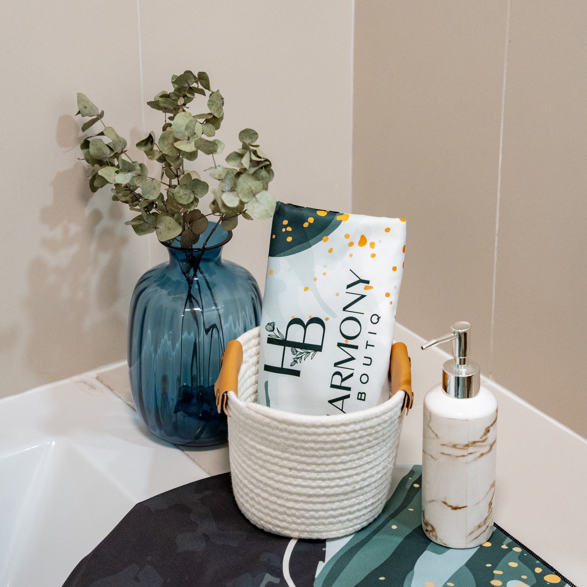 Rolled Emerald Mist face towel in a white decorative basket with blue vase and marble soap dispenser – spa-inspired setup.
