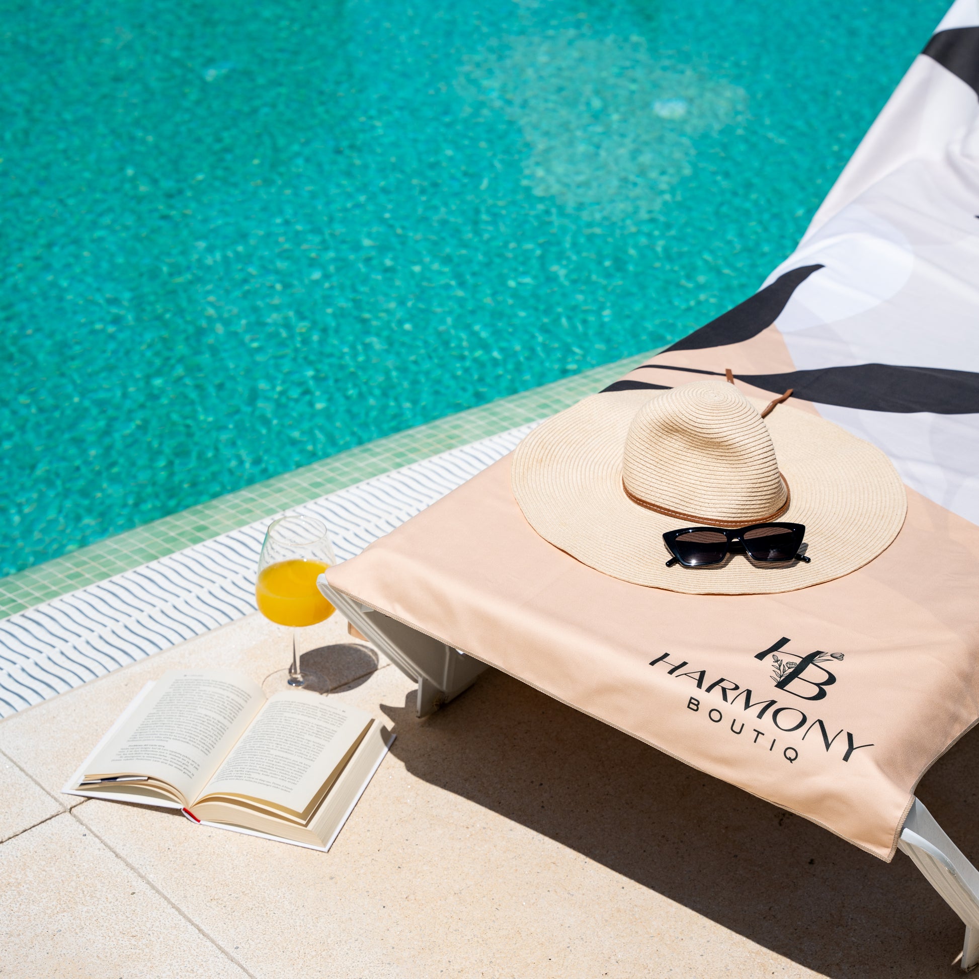 Ecovera beach towel spread over a lounger with sun hat, sunglasses and book beside a pool – ideal for vacation lounging.
