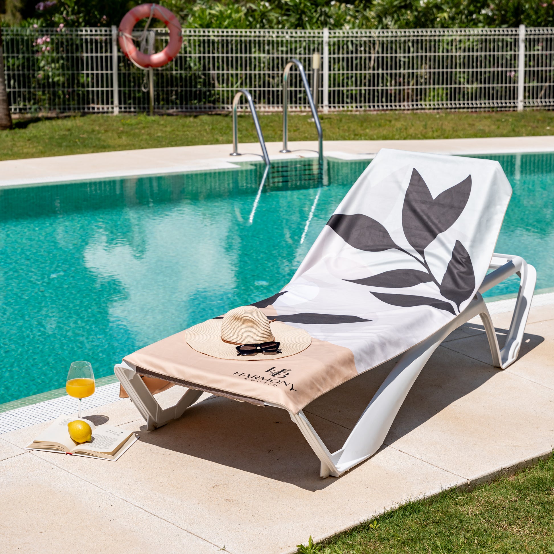 Full view of Ecovera towel on poolside lounger with sun hat, book and juice – stylish and practical beach day setup.
