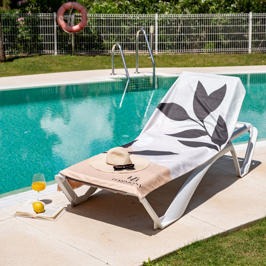 Full view of Ecovera towel on poolside lounger with sun hat, book and juice – stylish and practical beach day setup.
