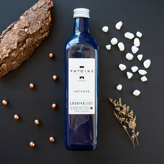 Antoine Intense laundry detergent surrounded by natural ingredients, showcasing oak moss and amber notes for an intense scent.