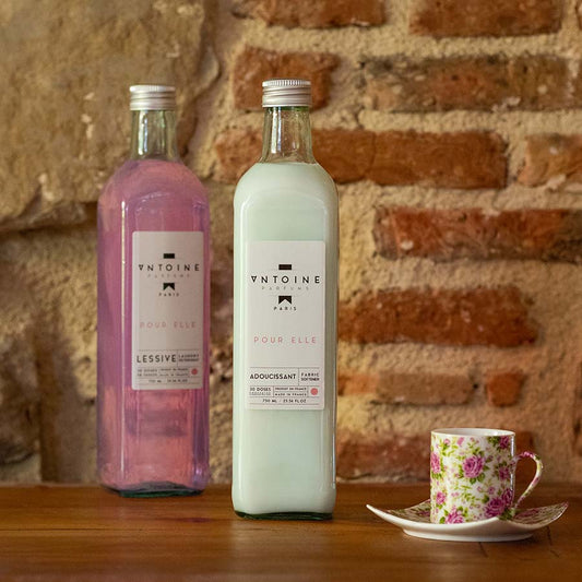 Antoine Pour Elle fabric softener in glass bottle, displayed in a warm rustic ambiance with elegant teacup