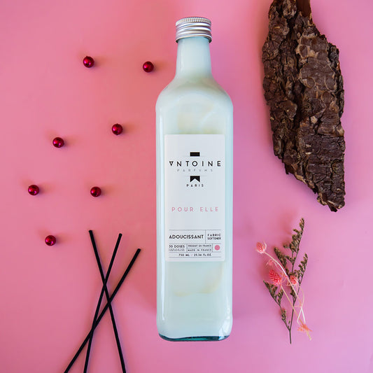 Antoine Pour Elle fabric softener with decorative elements on a pink background, showcasing the luxury and eco-friendly glass packaging.