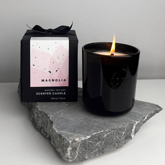 Magnolia scented candle in black glass jar with wooden lid on stone slab