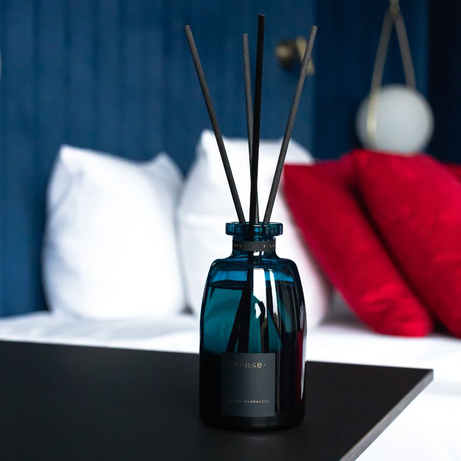 ODORO Sense Optimist fragrance diffuser in a cozy bedroom setting, complementing a navy-blue background and white pillows, bringing a sense of relaxation and style.