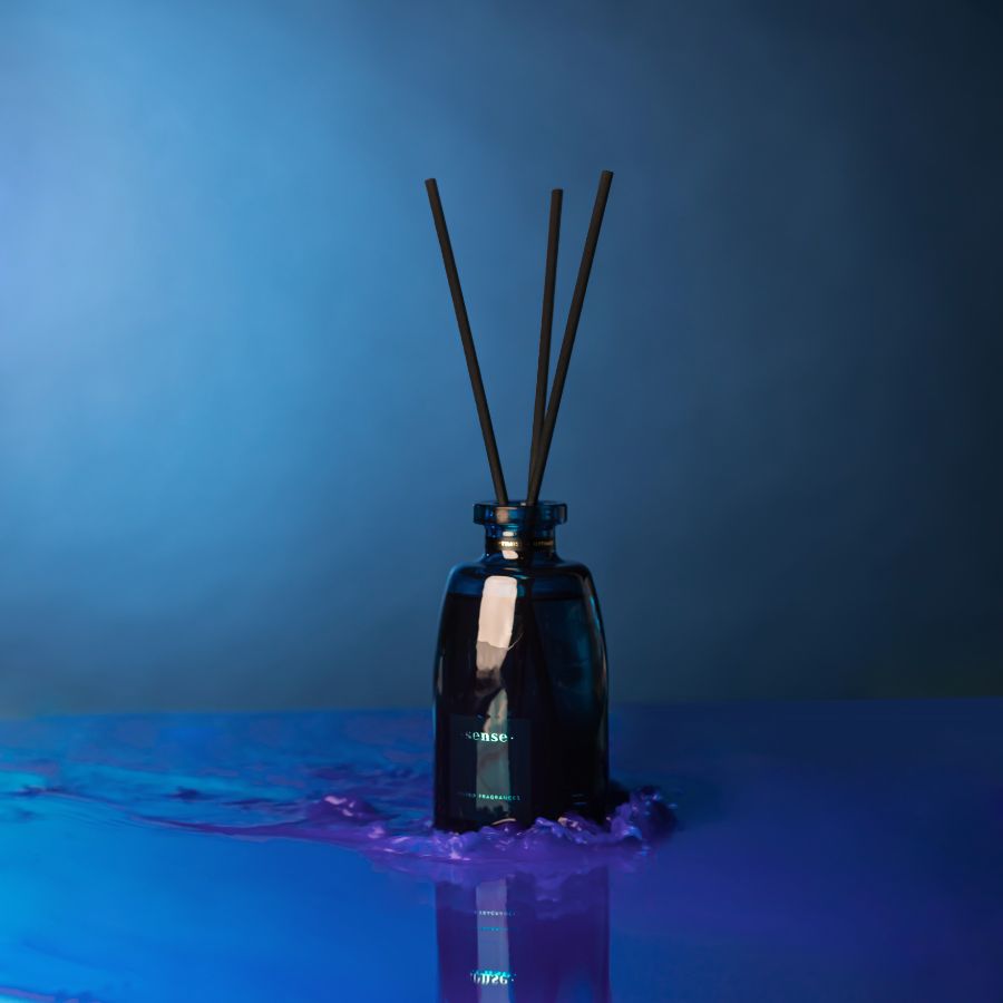 ODORO Sense Optimist fragrance diffuser with black reeds, placed on a surface reflecting a vibrant blue light, evoking a serene and confident atmosphere.