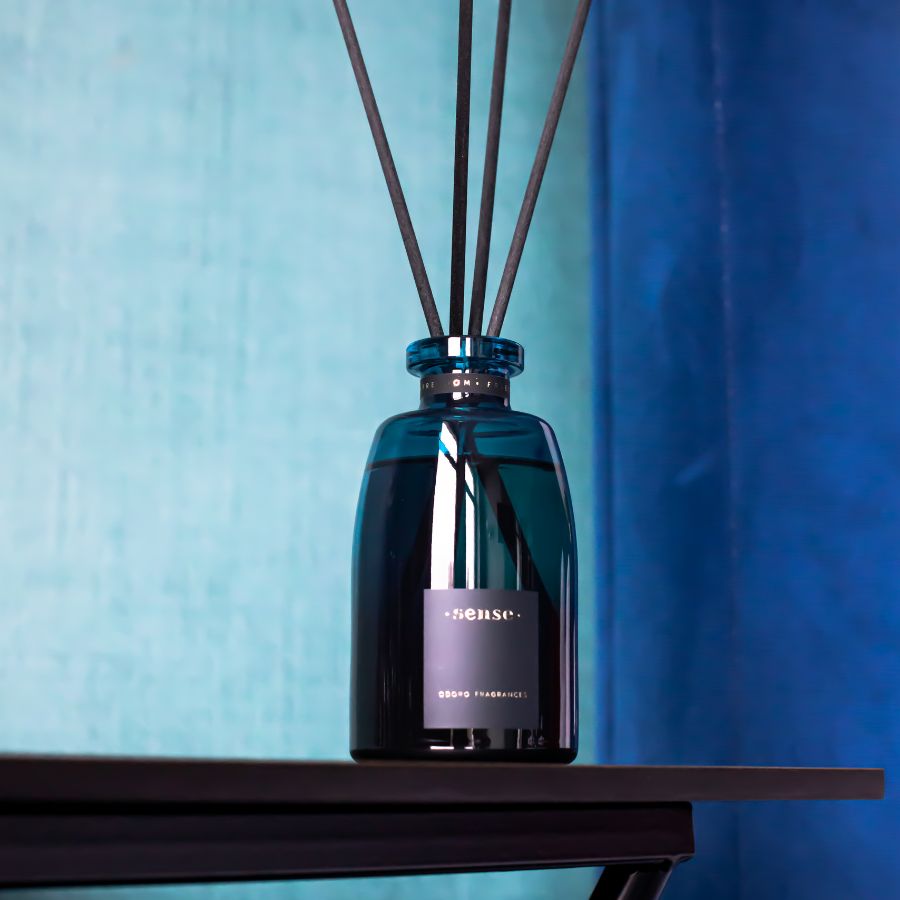 A close-up of ODORO Sense Optimist fragrance diffuser with black reeds, placed against a cool blue background, emphasizing its modern and sleek design.