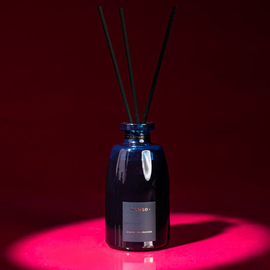 ODORO Sense Optimist fragrance diffuser with black reeds, placed against a dark red background, creating a moody ambiance.