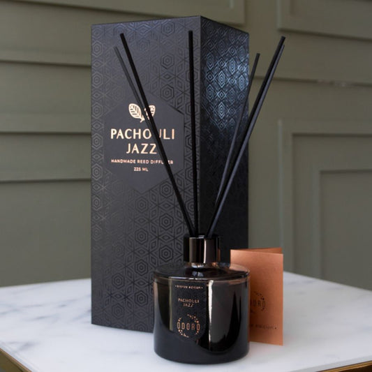 A stylish home fragrance bottle with reed sticks displayed in an elegant interior, alongside its luxurious cardboard packaging. The setup is on a white marble table against a rich khaki-colored wall, showcasing sophistication and modern aesthetics.